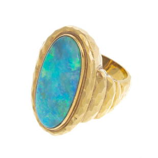 A Bold Opal Ring in 18K Yellow Gold: 18K yellow gold ring featuring an oval opal with mostly green and blue play-of-color, measuring 23 x 12 mm and weighing approx. 5.70 cts, bezel set, step shoulders, hammered finish with high polish,