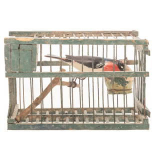 American Folk Art Bird In Cage: Early 20th century; green painted wood and metal wire cage housing carved and painted wood bird with wire legs, also pottery feeder, 5 in. H., 7 1/4 in. L., 4 1/2 in. W. All proceeds of the sale of th