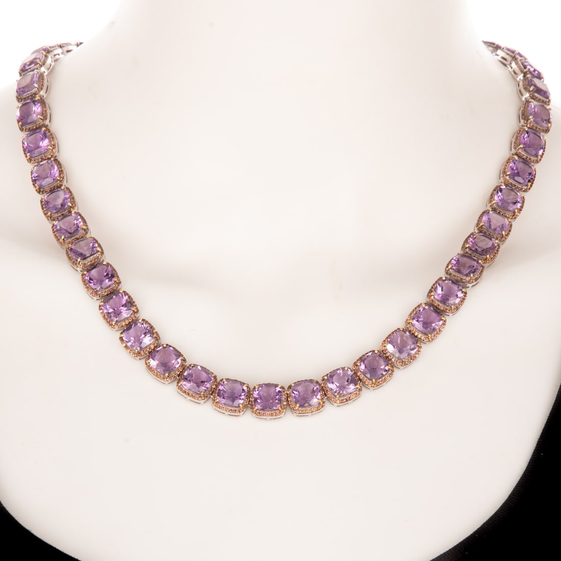 An Amethyst & Orange Sapphire Line Necklace in Sterling Silver: Sterling silver necklace featuring a line of cushion cut amethysts set in 14K yellow gold prongs weighing approx. 85.00 ctw individually prong set in the center of a halo of bead set round orange sapp