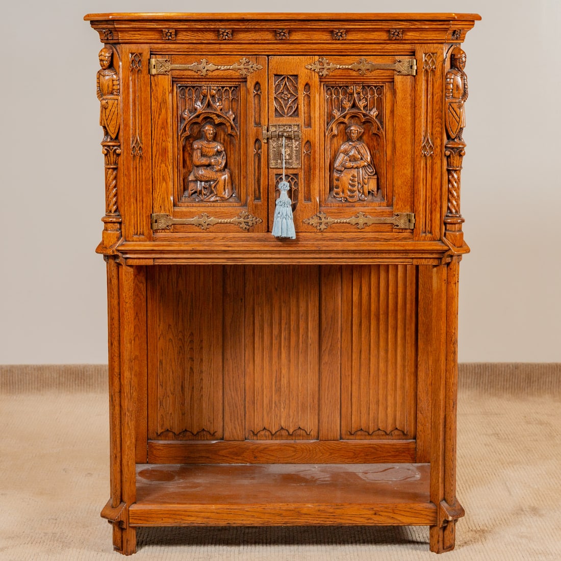 Gothic Revival Carved Oak Cabinet: Projecting cabinet over figural carved two door elevated cabinet flanked by carved knights supported by stylized columnar legs connected by an undershelf, 53 in. H, 38 in. W, 19 1/2 in. D