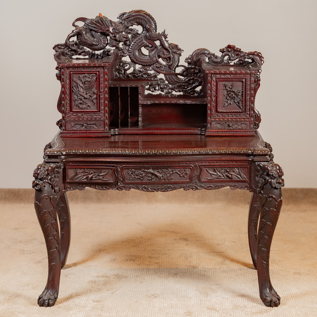 Chinese Carved Hardwood Writing Desk: Heavily carved throughout with dragon and nature motifs, the two door two shelf cabinet resting on a shaped and carved top over a matching three drawer apron supported by cabriole legs ending in paw f