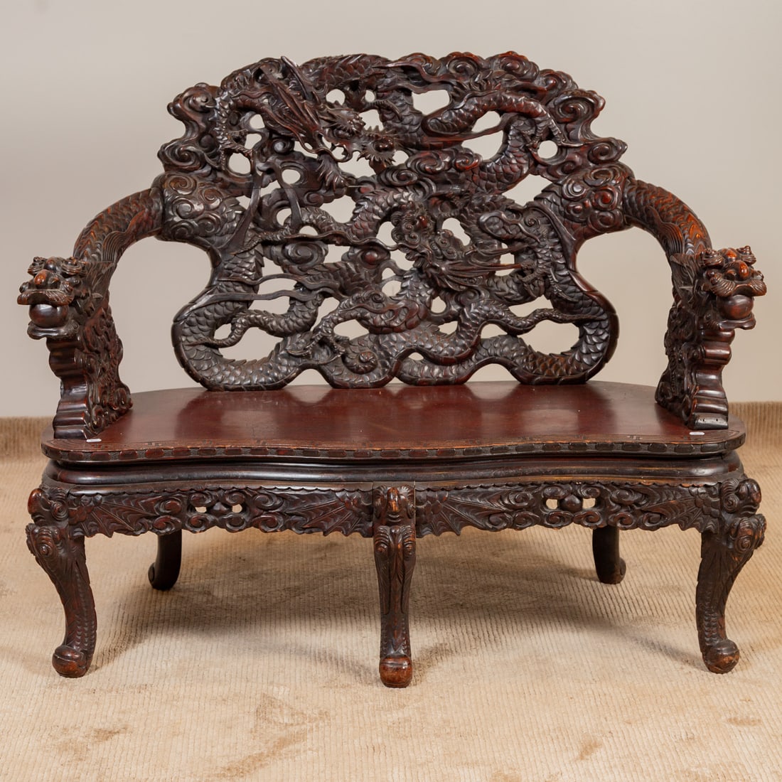 Chinese Elaborately Carved Hardwood Bench: The backsplat carved in the form of two dragons, extending into two dragon form arms, flat bench seat with carved apron supported by five carved legs, 42 in. H, 51 in. W, 24 in. D