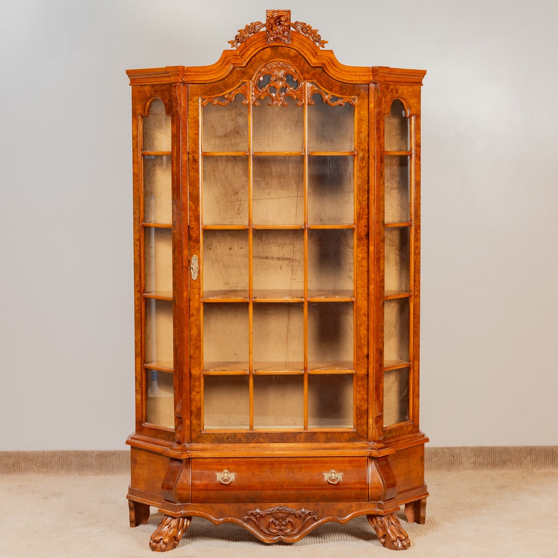 American Classical Style Walnut Display Cabinet: Shaped pediment with projecting cartouche over a glazed door cabinet resting on a one drawer bombe form base ending in ball and lion's paw feet, 82 in. H, 48 in. W, 16 in. D