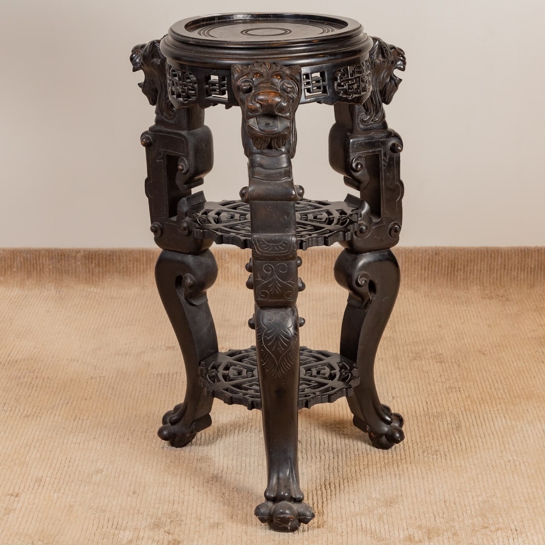 Chinese Ebonized Hardwood Jardiniere Stand: Circular stand with Foo Dog headed carved legs connected by a pair of matching undershelves ending in lion paw feet, 39 in. H, 24 in. Diam.