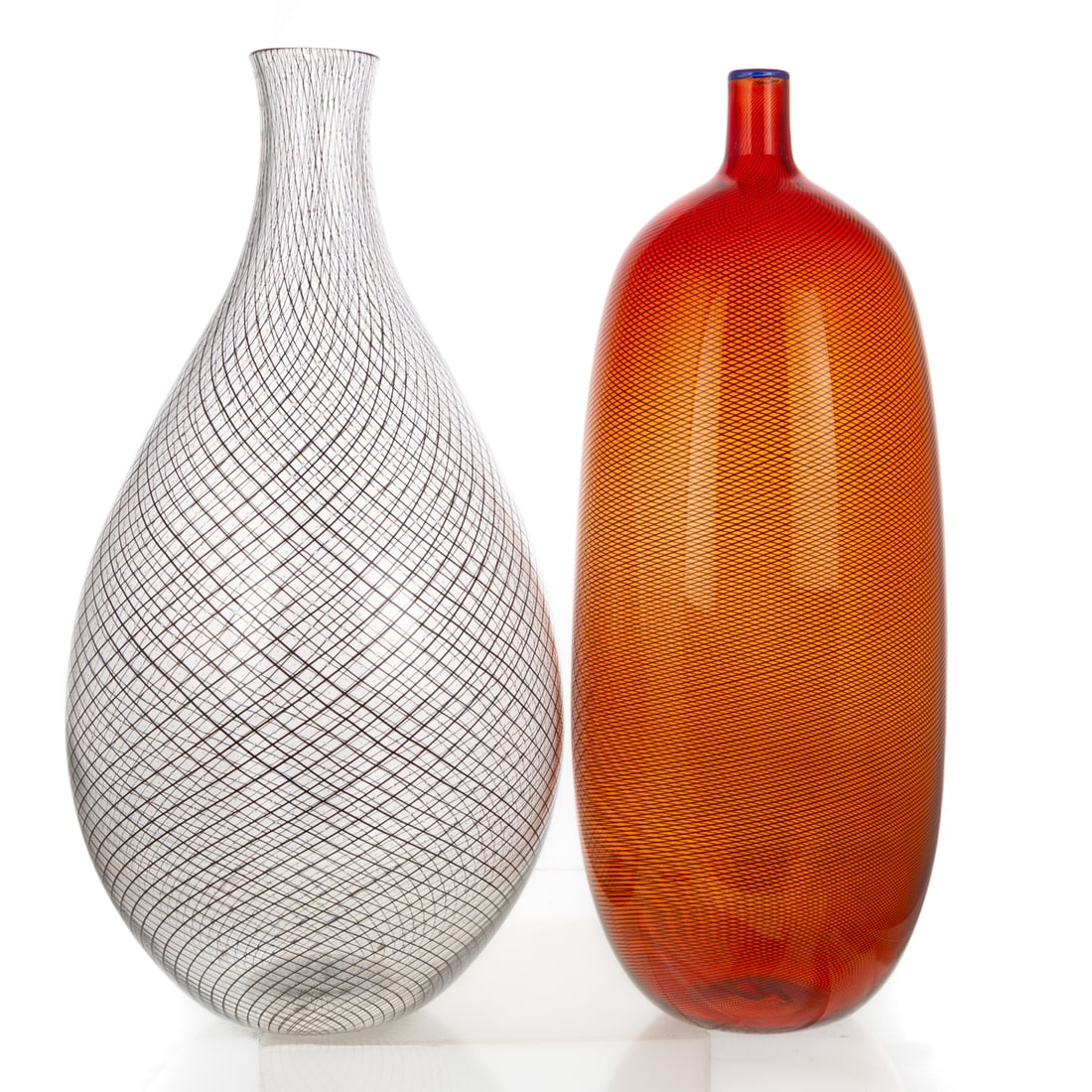 A Bottle-Form & a Reticello Art Glass Vase: Includes a colorless reticello vase with black reticello and centered pieced air bubbles, illegibly signed on bottom, 15 3/4 in. H, approx. 7 1/2 in. Diam.; and an orange/red translucent bottle-form a