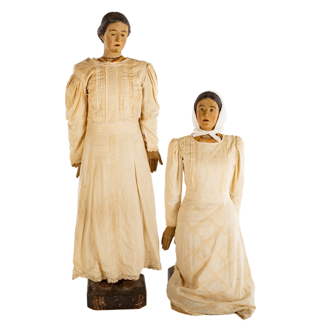 Two Spanish Colonial Female Religious Articulated Figures: Two polychrome wood Spanish Colonial articulated female religious figures in Victorian clothing, one is kneeling and praying, 38 in. H, 15 in. W, approx. 14 in. D; the other stands giving the hand