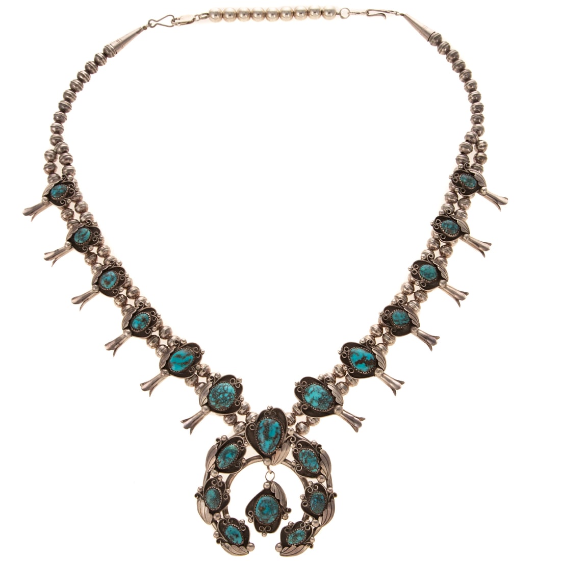 A Navajo Morenci Turquoise Squash Blossom Necklace in Sterling Silver: c.1977, Sterling silver squash blossom necklace, Navajo, featuring well matched oval and pear shape Morenci spider web turquoise set into Naja and squash blossoms, signed "A/I," hook clasp with remova