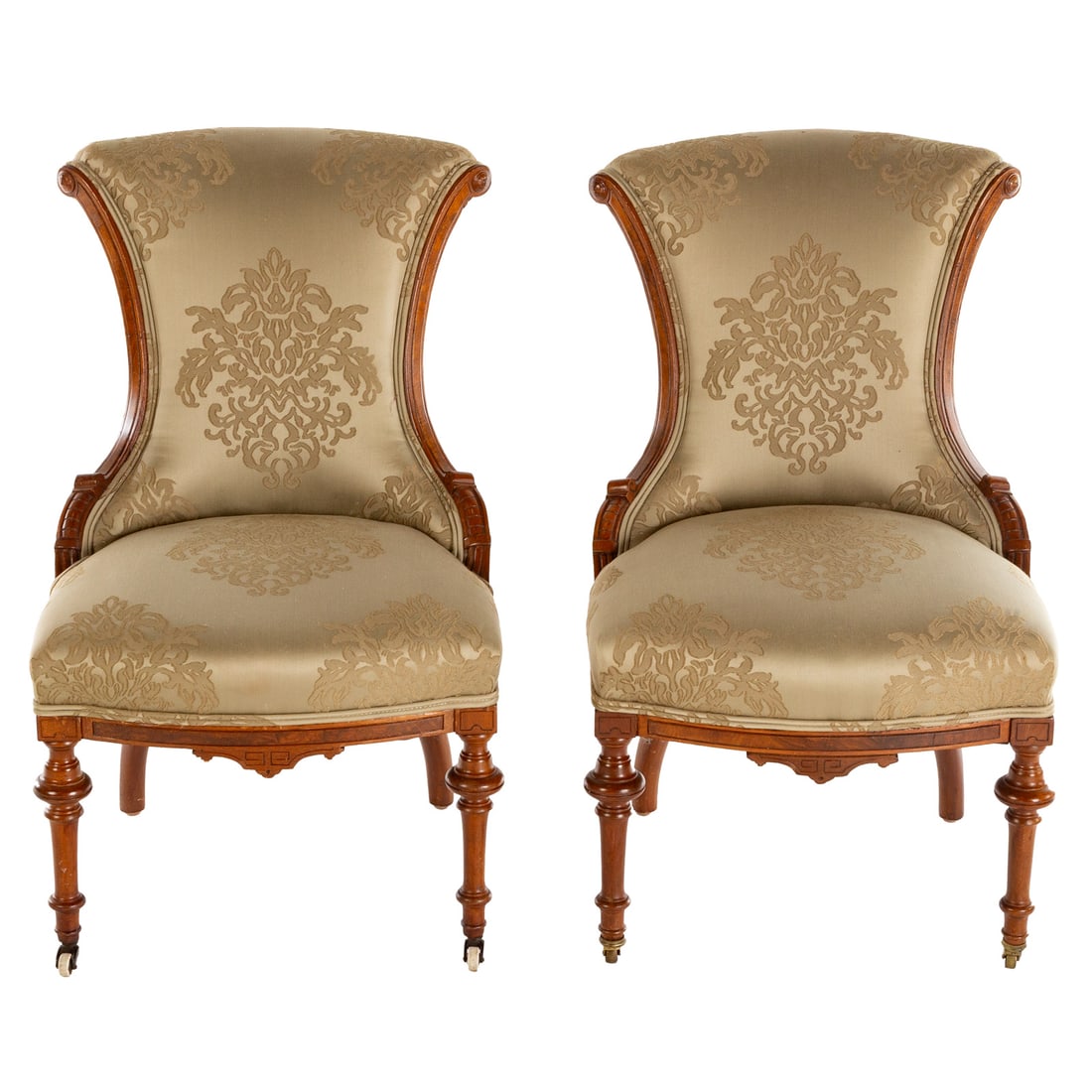 A Pair of Eastlake Victorian Carved Walnut Chairs: Silk damask reupholstered backs and seats, carved curvelinear stiles, matching aprons ending in turned and castered feet, each: 33 1/2 in. H, 20 in. W, 19 in. D