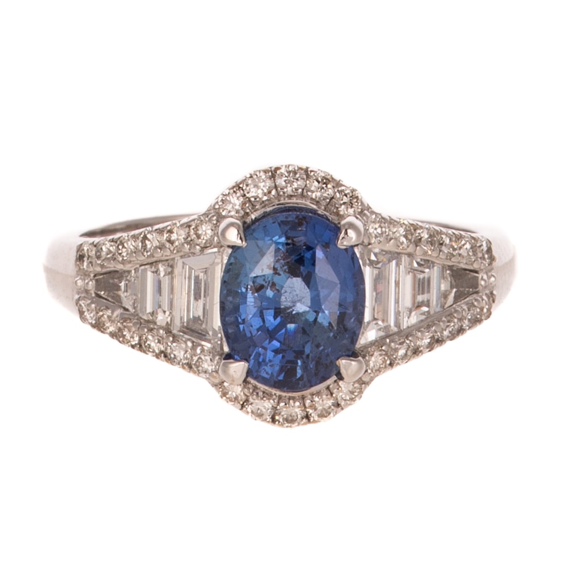 A 1.60 ct Sapphire & Diamond Ring in 18K: 18K white gold ring featuring an oval shaped sapphire weighing approx. 1.60 cts prong set with baguette diamonds channel set on shoulders all surrounded by a round diamonds shared prong set, all diamo