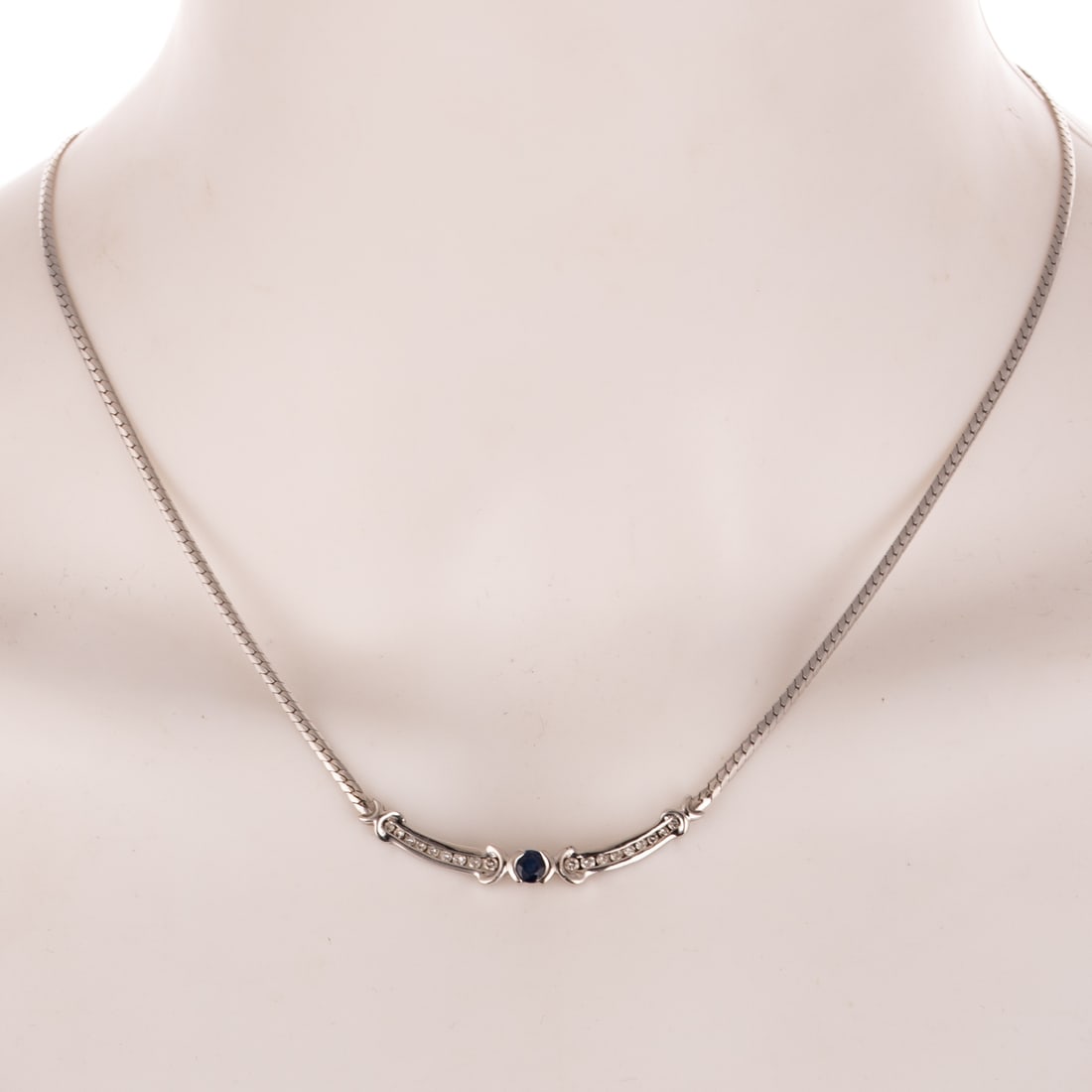 A Sapphire & Diamond Necklace in 14K: 14K white gold necklace featuring a round sapphire weighing approx. 0.30 ct semi-bezel set flanked by round diamonds weighing approx. 0.15 ctw channel set with an integrated herringbone chain,