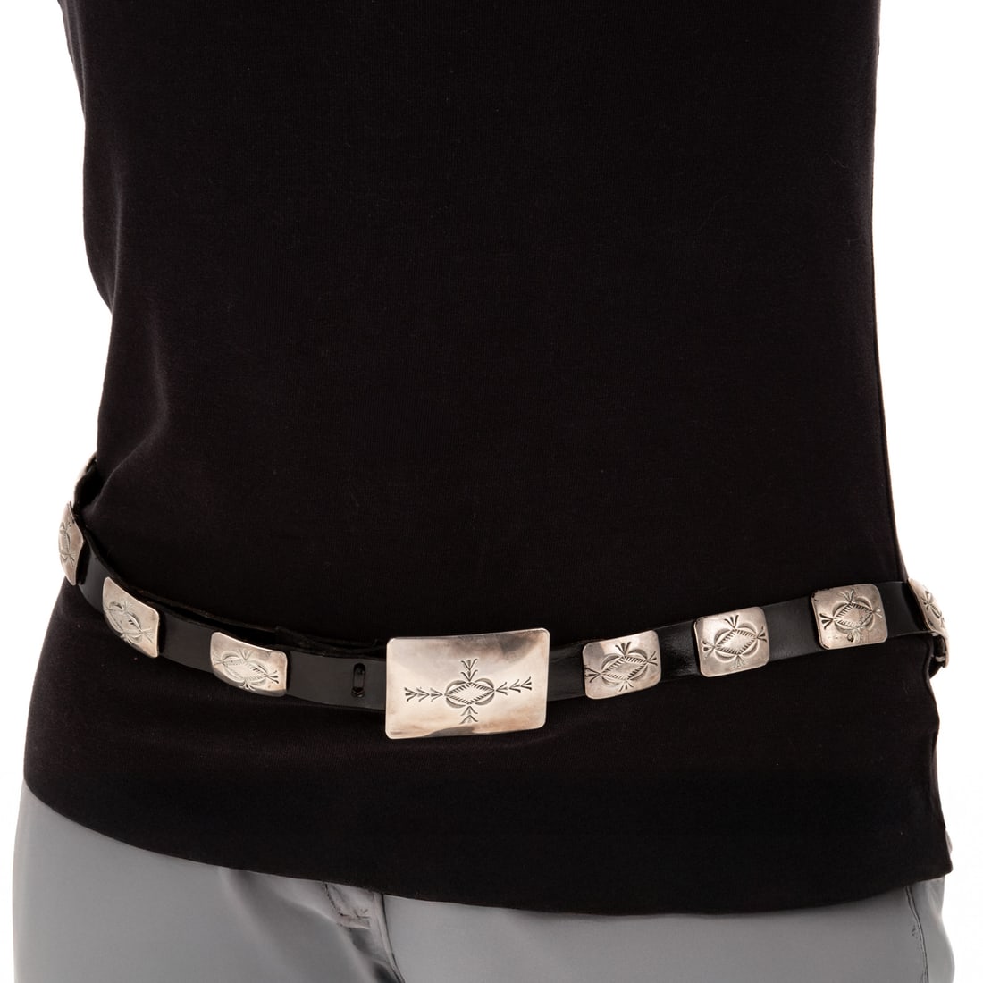 A Vintage Navajo Concho Belt in Sterling Silver: Sterling silver concho belt made by Navajo artists designed with 20 rectangular hand stamped conchos on a black leather belt, larger hand stamped rectangular buckle, 44 in. L, 208.8 grams Provenance: 