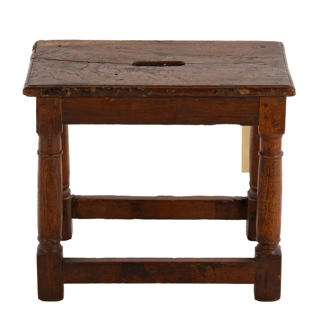 Louis XIII Oak Stool: First half, 17th century, carved out handle in molded top, supported by turned columnar legs connected by a rectangular stretcher, 18 in. H, 20 1/2 in. W, 12 in. D Provenance: Provenance available