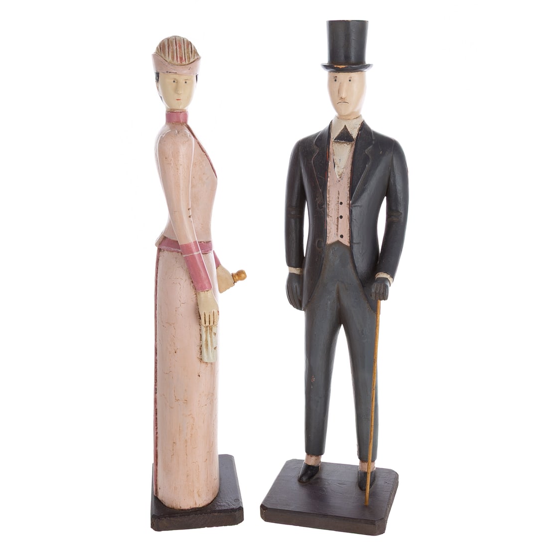 Two Haberdashery Folk Art Display Figures: A pair of carved wood Edwardian Haberdashery display figures in Victorian attire. Figures sit atop wooden flat bases. Man holding a walking stick, man: 24 1/2 in. H, 6 1/2 in. W, approx. 5 3/4 in. D,