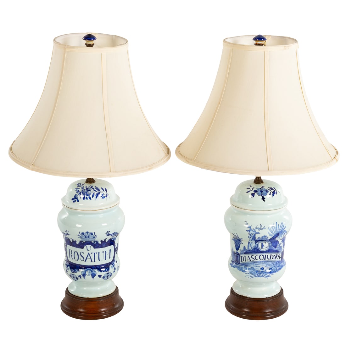 A Pair of Dutch Delft Apothecary Lamps: A pair of blue and white hand-painted tin glazed earthenware Dutch Delft apothecary jars mounted as lamps on wooden bases, one with scrolling cherub and peacock motifs framing a bold cartouche