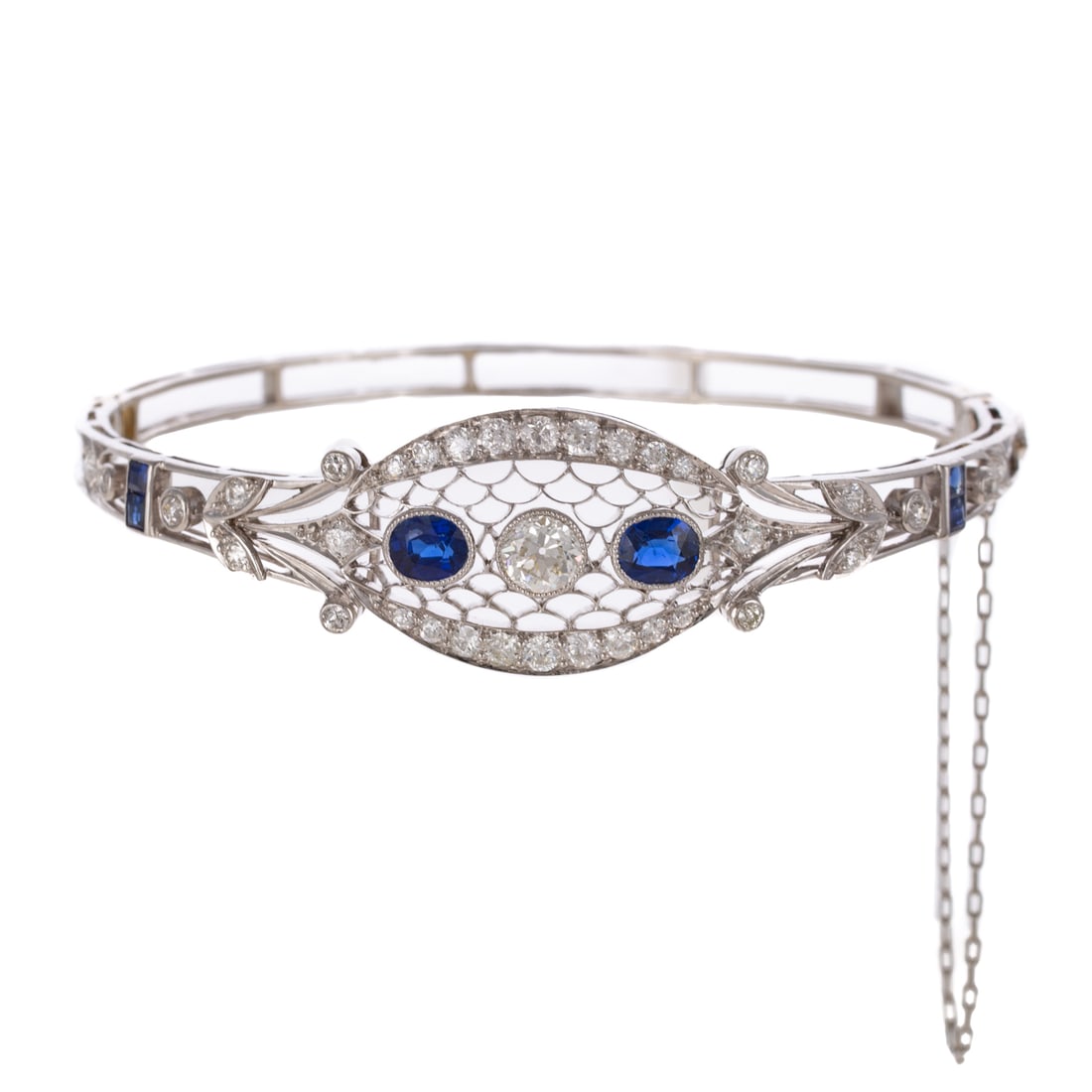 An Edwardian Diamond & Sapphire Bangle in Platinum: c.1900s, platinum oval hinged bangle bracelet featuring a central Old European cut diamond weighing approx. 0.45 carats with two larger oval fine blue sapphires weighing approx. 0.80 ctw set in open l