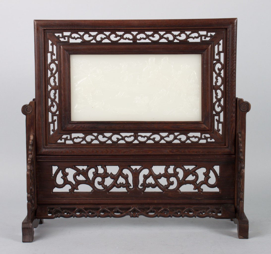 Chinese carved wood table screen with jade plaque: inset mutton-fat jade plaque depicting scholars writing a scroll in garden, set in Chinese carved hardwood stand, 13 in. H., 13 in. W. at base
