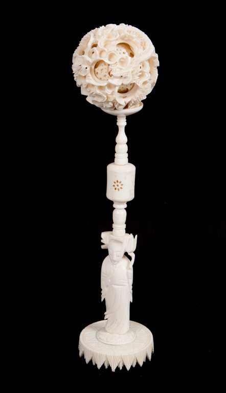 Chinese carved ivory puzzle ball: modeled as entwined dragons with a carved bone figural stand, modeled as Quan-Yin on lotus flower
