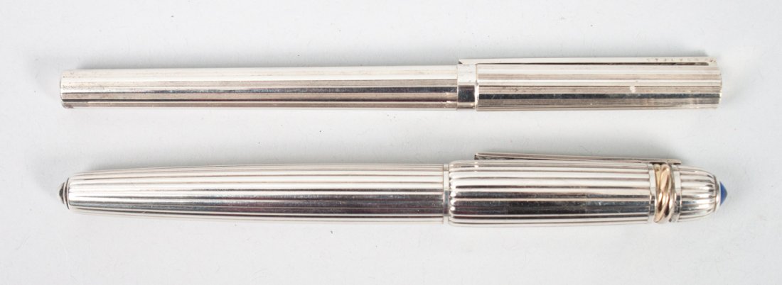 Two French collectible pens: 1.) Pasha de Cartier ballpoint pen with a silver body and blue cabochon spinel atop the cap, marked 1988 1227, 2.) S T Dupont fountain pen with a silver body and 18 karat yellow gold nib, serial #57JL