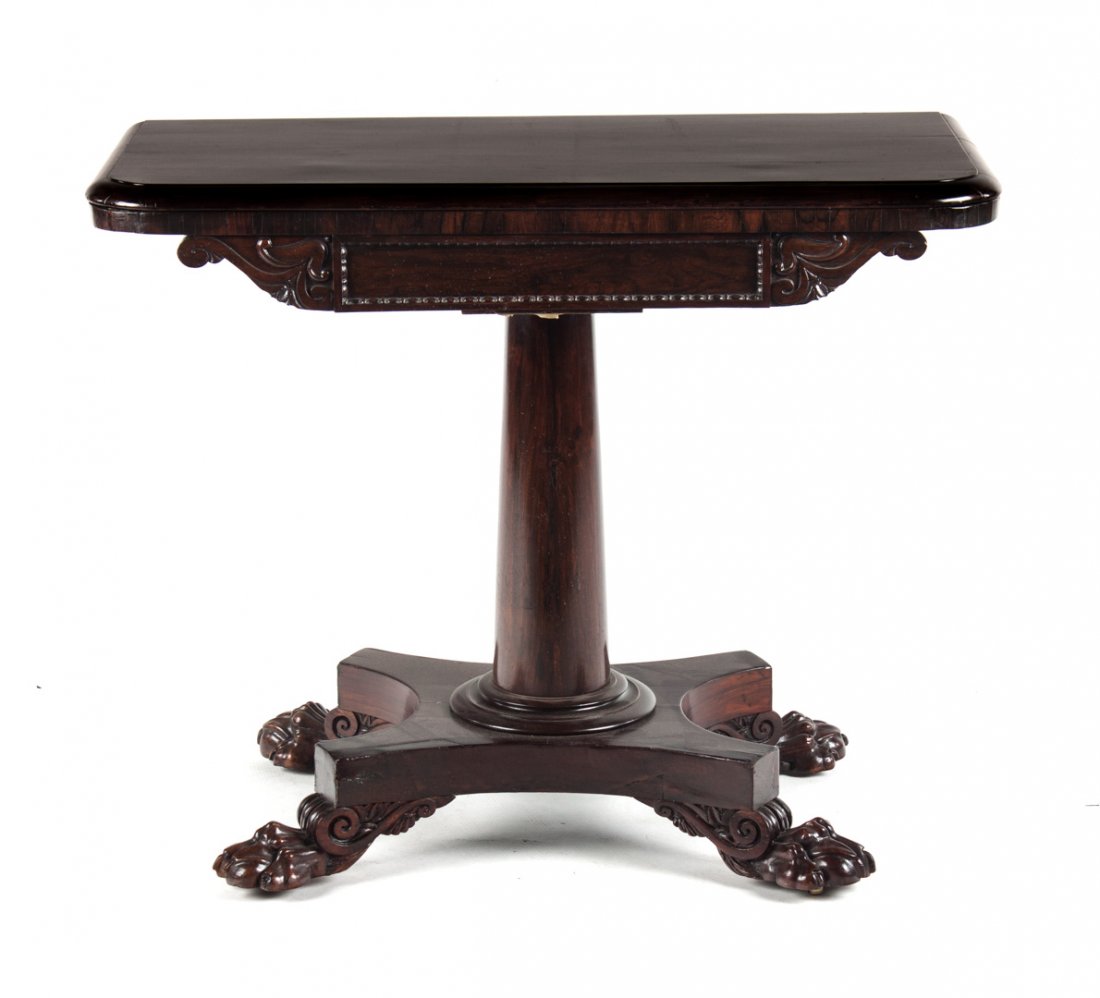 George IV rosewood flip-top games table: circa 1820; revolving beize-lined flip top with foliate carved apron on columnar shaft with paw-foot platform base, 29 in. H., 36 in. W., 18 in. D.