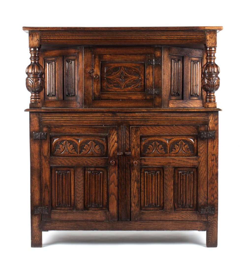 Tudor Revival oak court cupboard: late 19th/early 20th century; faceted carved top section with cup and cover baluster supports, base with carved panel doors, 54 in., 48 in. W., 18 in. D.