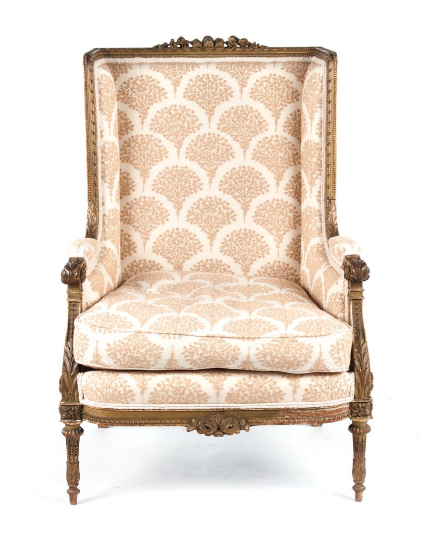 Louis XVI style giltwood wing-back bergere: late 19th/early 20th century; floral and foliate carved exposed giltwood frame, upholstered paneled back, arms, seat and loose seat cushion, fluted foliate carved feet, 41 in. H., 28 in. W., 28 in. D.