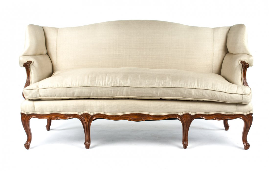 Louis XV provincial style upholstered settee: Curved crest rail, upholstered back, winged arms and seat over half- frame with loose seat cushion, exposed scroll carved arms, apron, and cabriole legs, 34 1/2 in. H., 36 1/4 W., 22 in. D.