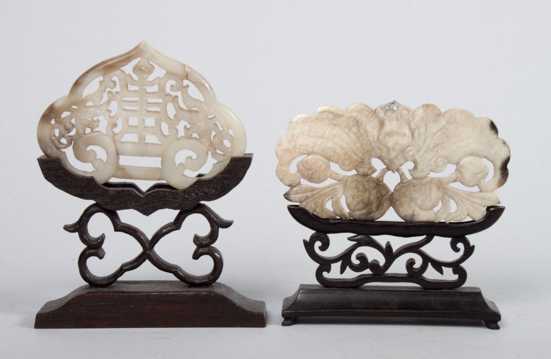 Two Chinese carved mutton fat jade amulets: one carved as bats with calligraphy, other carved as large bat with pomegranate, each with wood display stand, each 3 1/2 in. W.