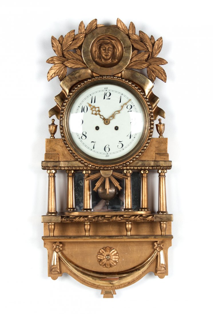 French Empire style giltwood wall clock: cornice with circle having mask medallion flanked by leaf clusters, clock with temple support with Corinthian columns base with rosettes and swag decoration, 32 in. L., 16 in. W.