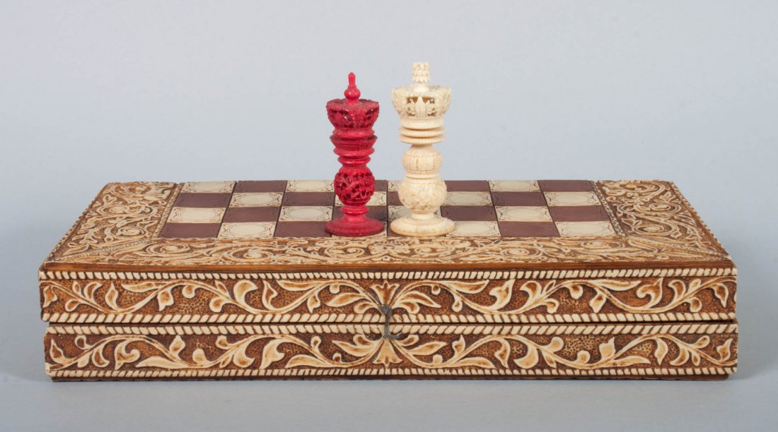 Chinese carved ivory chess set: white and dyed red carved ivory chessmen, with folding board/case and dyed ivory squares, border elaborately carved ivory veneer of scrollwork and fanciful beasts, king figure - 4 in. H., board - 15 i