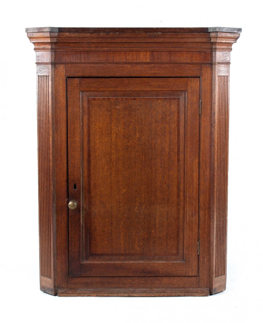 George IV carved oak hanging corner cupboard: early 19th century; flat top with molded cornice, compartment with shaped drawers enclosed by solid panel door with fluted pilaster supports, 49 in. H., 48 1/2 in. W., 21 1/2 in. D.