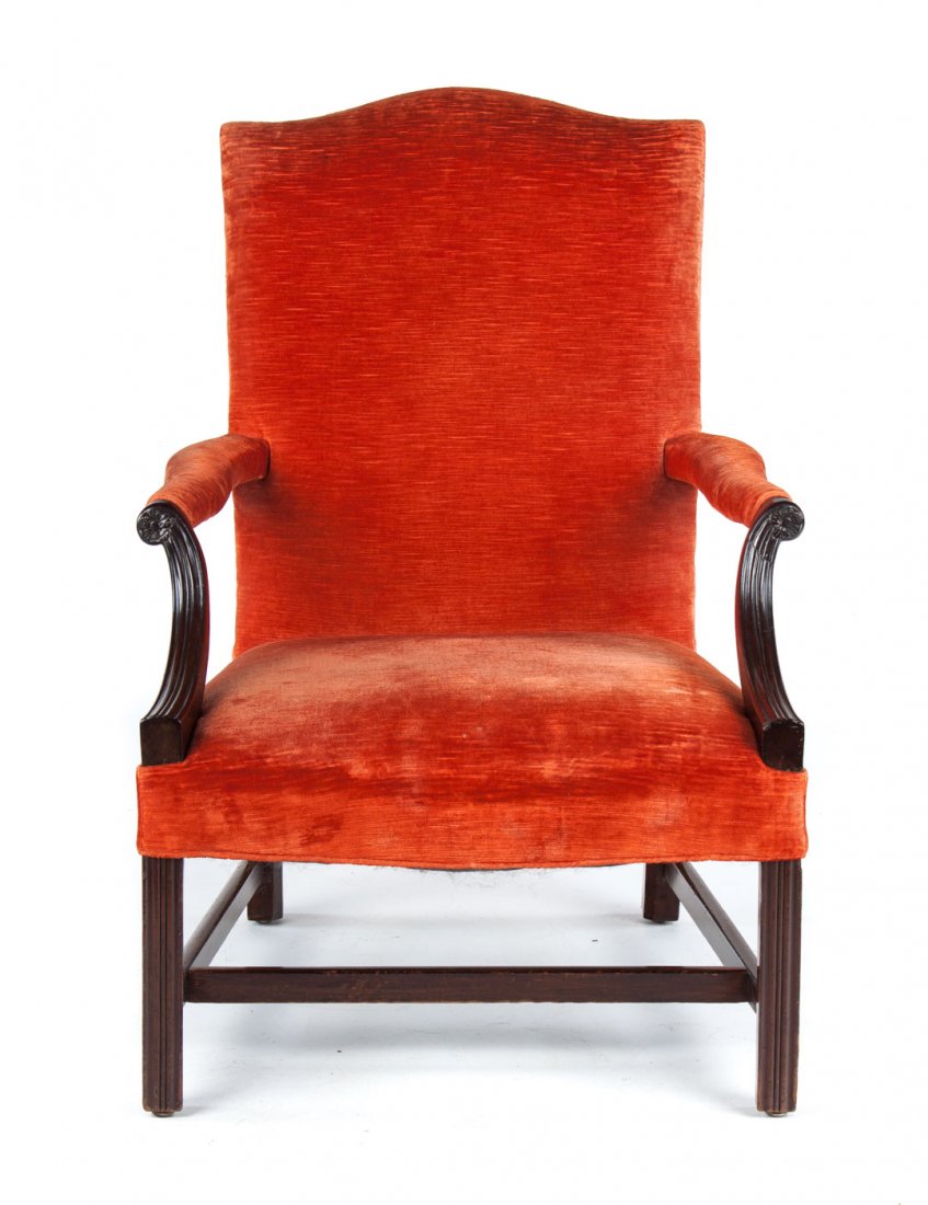 George III carved mahogany lolling chair: circa 1770; serpentine crest rail, upholstered panel back, arms, and seat over frame, molded rosette carved recessed arms, molded chamfered legs connected by stretchers, 41 in. H., 27 1/4 in. W., 24 i