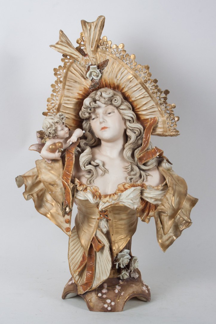Teplitz bust of beauty with cupid: early 20th century; modeled as young beauty in lace trimmed hat and flowers with cupid, stamped mark, 25 in. H.