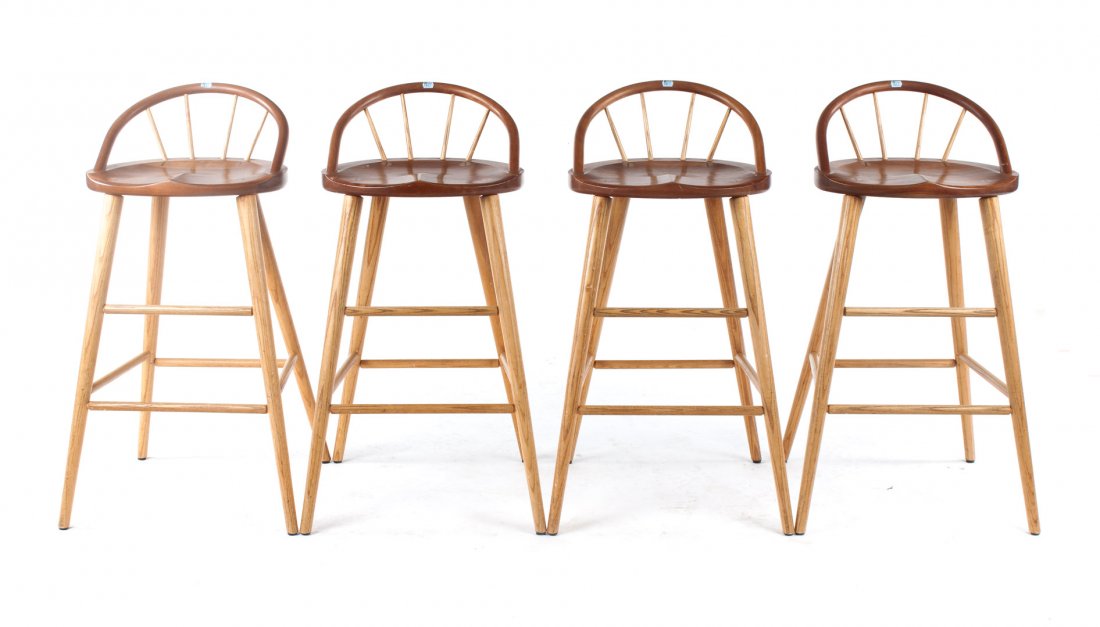 Four Thos. Moser cherry and oak bar stools: 20th century; shallow curved spindled backs, sculpted plank seats, round splayed legs connected by stretchers, 38 in. H., 18 in. W., 14 in. D.