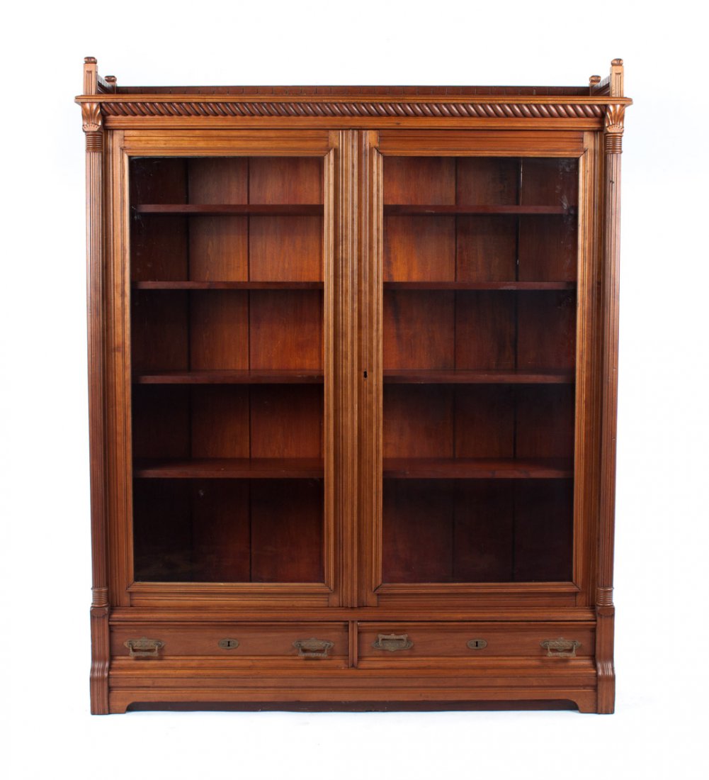 Eastlake style maple bookcase: circa 1880; flat top with rope-turned cornice and 4 in. raised gallery edge, compartment with shelves enclosed by double glass panel doors, two medium long drawers beneath, reeded columnar supports, 6