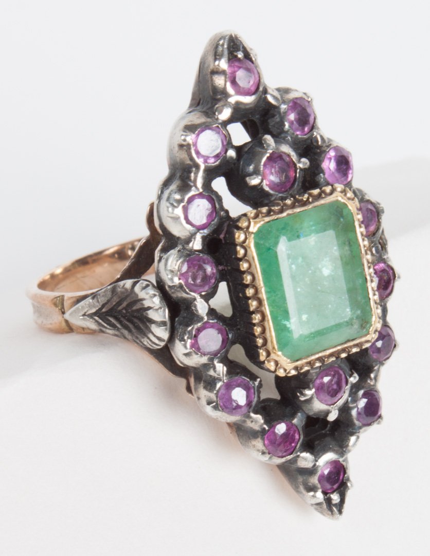 Victorian Arabesque style emerald and ruby ring: centering an emerald, 9 X 7 X 6 mm., surrounded by small rubies, held in a silver setting, the shank tests as 10K, 10 grams; size 7 3/4