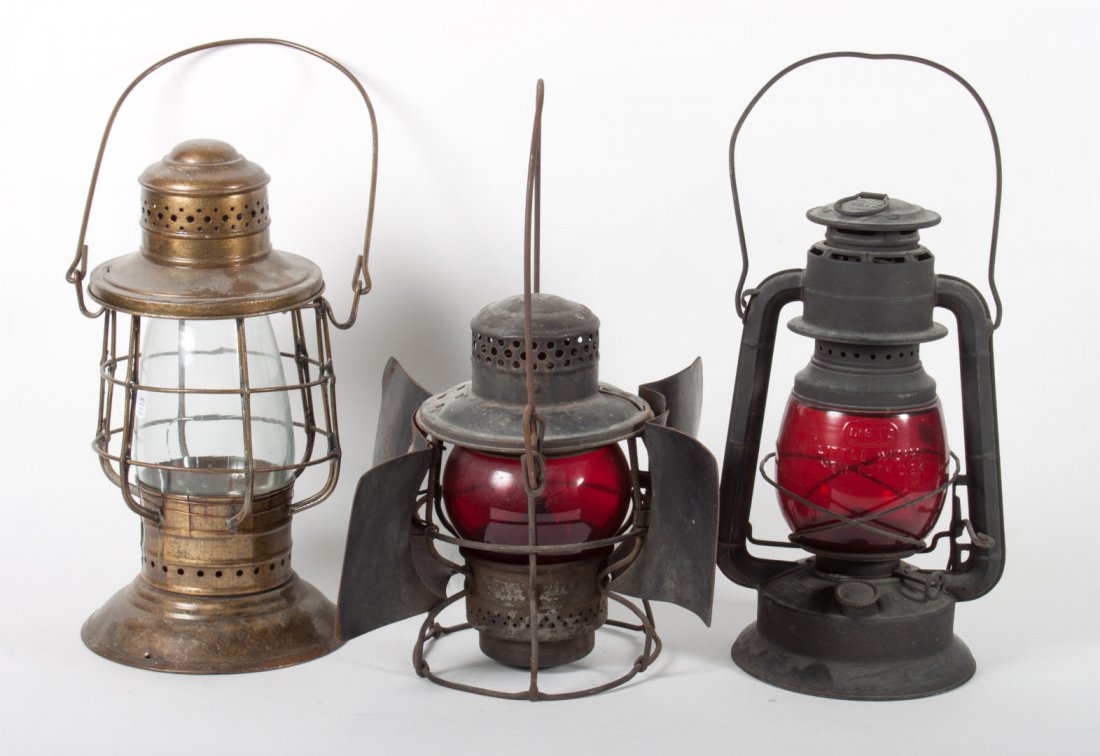 Three railroad signal lanterns: One "Pennsylvania Railroad"," sheet metal with ruby glass globe, similar Dietz "Little Wizard" lantern, and sheet metal and clear glass glove lantern