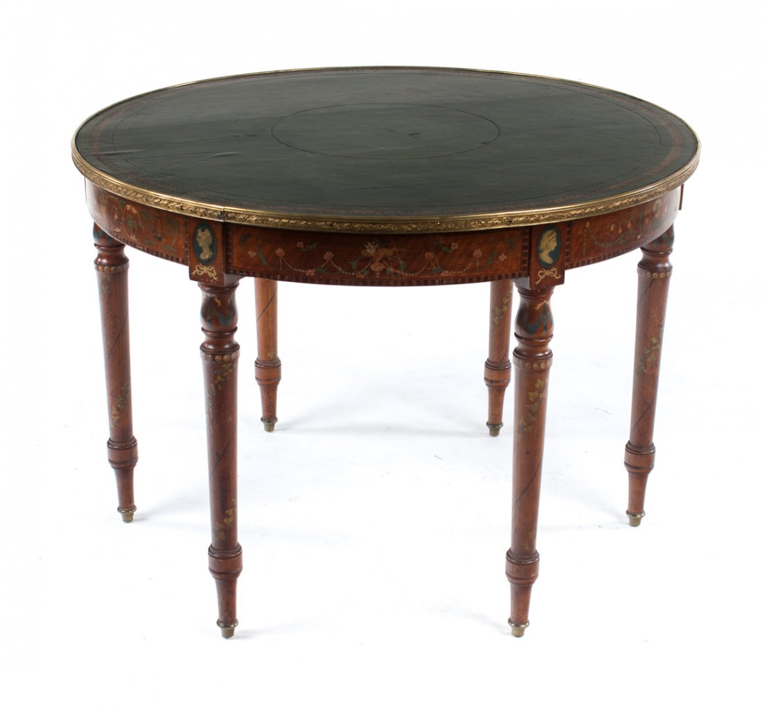 Edwardian paint decorated leather top table: Adam style, late 19th/early 20th century; 40 in. round gilt tooled leather top with stamped brass edge, apron with painted arabesques and profile medallions, six turned and tapered legs, painted flora