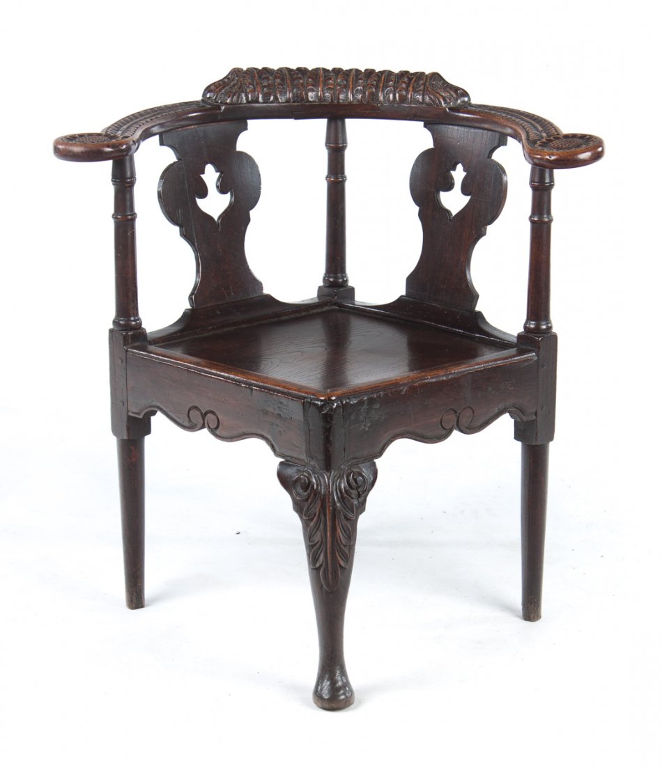 George III carved elmwood corner chair: late 18th century; rounded sunflower carved arms with double vasiform splats, plank seat, cabriole front leg with scroll carved knee, 29 in. H., 24 in. W., 18 in. D.