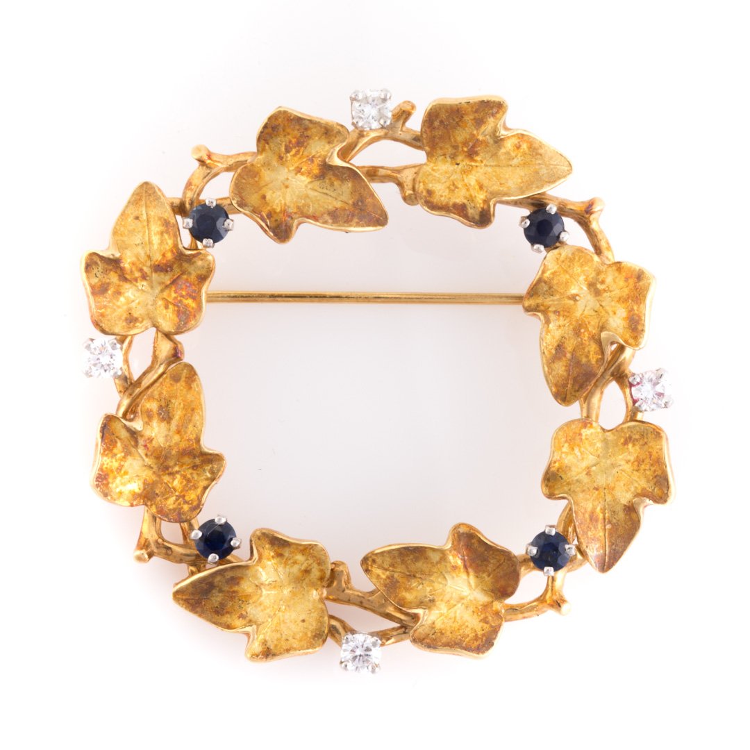 A Sapphire & Diamond Wreath Brooch by McTeigue: 18K yellow gold and platinum open circle leaf brooch by McTeigue & Co. with alternating round sapphires and diamonds, traditional pin closure, 1 5/8 in. Diam., 12 grams