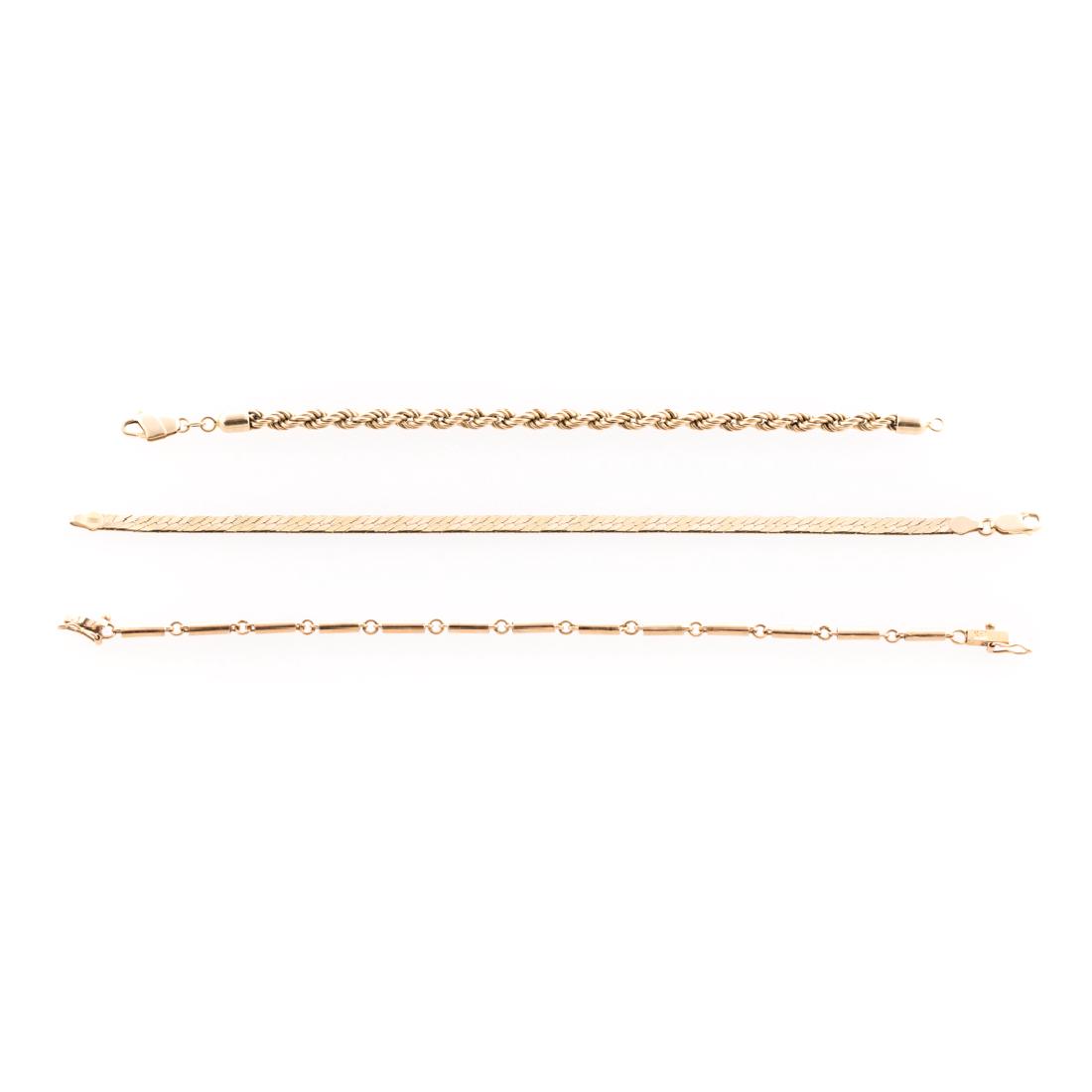 A Trio of Lady's Gold Chain Bracelets: 1) 18K yellow gold bar link bracelet with box clasp and figure 8 safety, 7.5 in. L, 2) 14K yellow gold twist rope bracelet with lobster clasp, 7 in. L and 3) 14K yellow gold herringbone chain bracelet