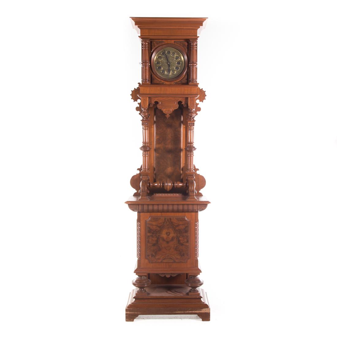 German Baroque style carved walnut tall case clock: late 19th century; works with brass dial enclosed by bonnet with flat molded cornice and carved pilaster supports, open waist with turned columns, base with burled panel on round turned feet on platfo