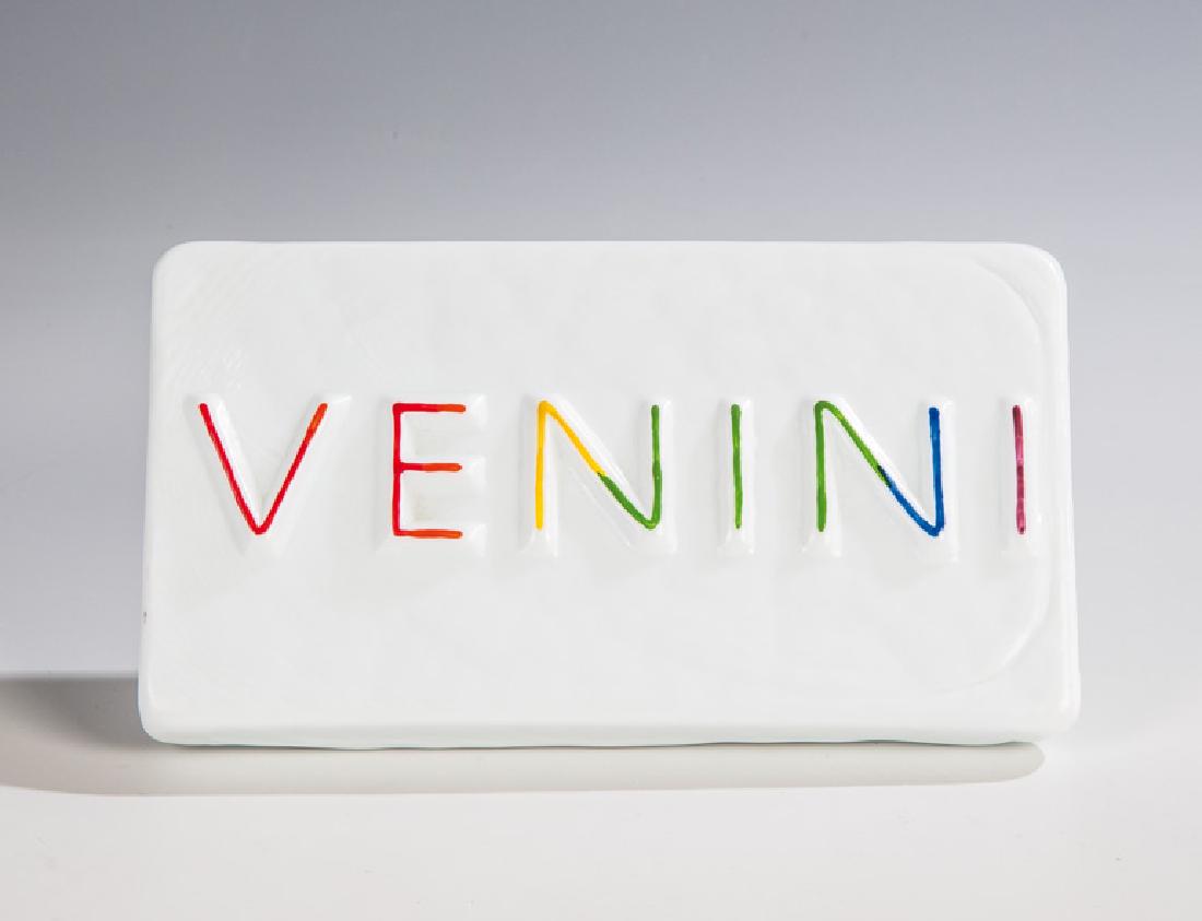 Firmenschild ''VENINI'': Firmenschild ''VENINI'' Venini, Murano Opakes Milchglas ('lattimo'), formgeschmolzen. Bunt bemalt. Metallmontierung. 9 x 16 cm Firmenschild "VENINI" Venini, Murano Opakes Milchglas ('lattimo'), formge