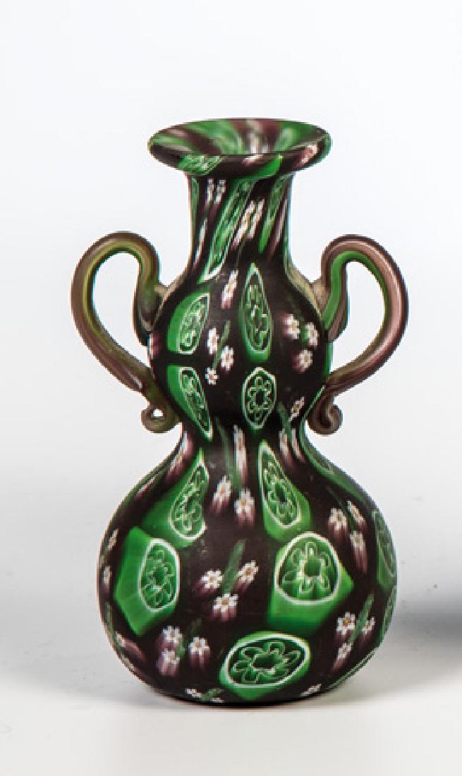 Zierhenkelväschen ''A Murrine floreali'': Zierhenkelväschen ''A Murrine floreali'' Fratelli Toso, Murano, um 1910 Farbloses Glas mit eingeschmolzenen mehrfarbigen Murrine. Oberfläche säuremattiert. Mündung min. best.. H. 11 cm Zierhenkelv