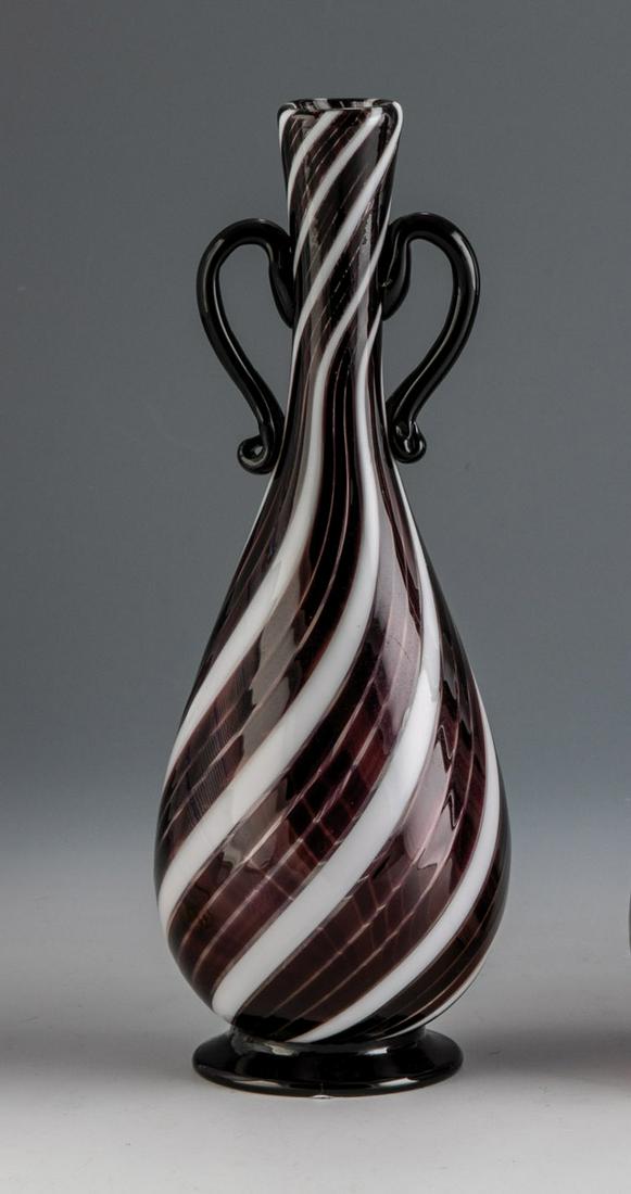 Henkelvase ''A Canne'': Henkelvase ''A Canne'' Dino Martens (Entwurf), Aureliano Toso, Murano, um 1955 Farbloses Glas, mit diagonaler Bandeinschmelzung ('a canne') in Violett und WeiÃŸ. Angesetzter FuÃŸ und Henkelapplike