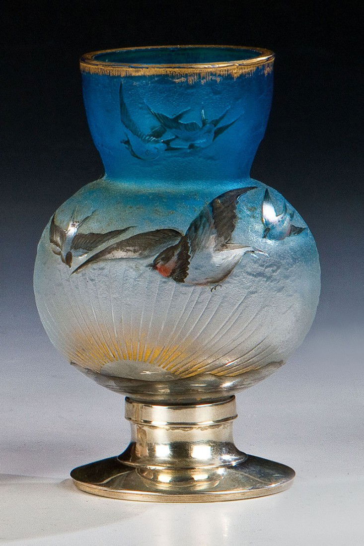 Kleine Vase mit Silbermontierung: Kleine Vase mit Silbermontierung Daum Frères, Nancy, um 1900 Farbloses, innen verlaufend blau unterfangenes Glas. Umlaufend in flachem Relief geätzter und mit buntem Email bemalter Dekor: Gebirgslan