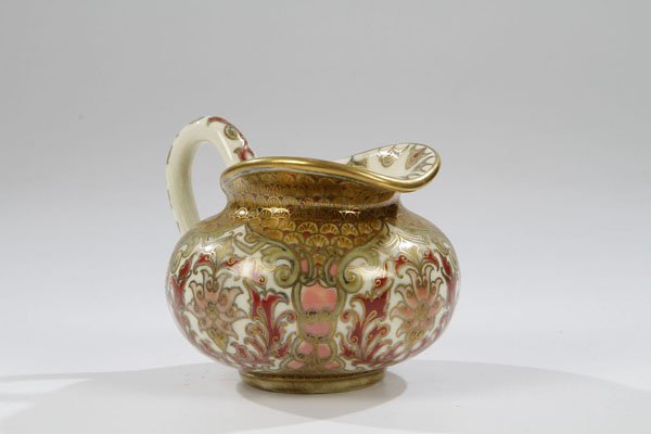 Kleiner Krug: Kleiner Krug Zsolnay, Pecs, um 1880 Steingut. Farbiger stilisiert floraler und ornamentaler Unterglasurdekor in umlaufendem Rapport. Konturen- und Binnenzeichnung in Gold. Unterglasurblauer Manufaktur