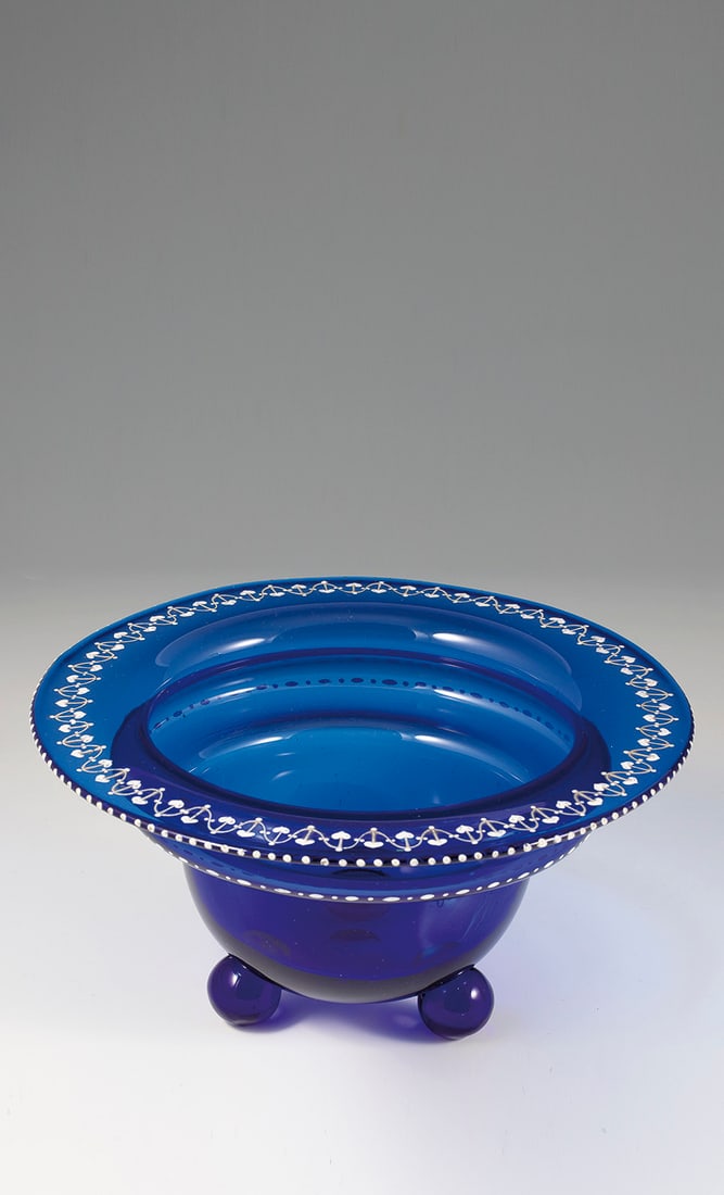 Foot shell: Foot bowl Loetz Wwe., Klostermühle, c. 1915 Cobalt blue glass with white opaque enamel painting. Decor: Leaf and flower stylization. Three attached ball feet. h. 11 cm; d. 21.5 cm. Lit.: Lötz - Böh