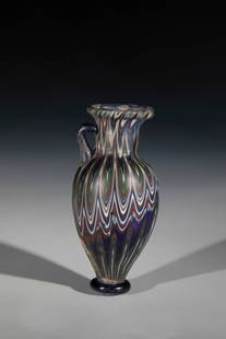 Amphoriskos: Amphoriskos probably Hellenistic-Roman cobalt blue glass with combed threads in white, rust-brown tones and green. Pressed disc as sand. Amphora shape with an appliquéd handle. Protruding lip rim