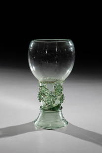 Roman: Romans, Germany or Netherlands, 17th century. Light green glass with tear-off. Woven foot. On the shaft, which is open at the top, two rows offset by appliquéd berry nubs. Below the bulbous cuppa, a