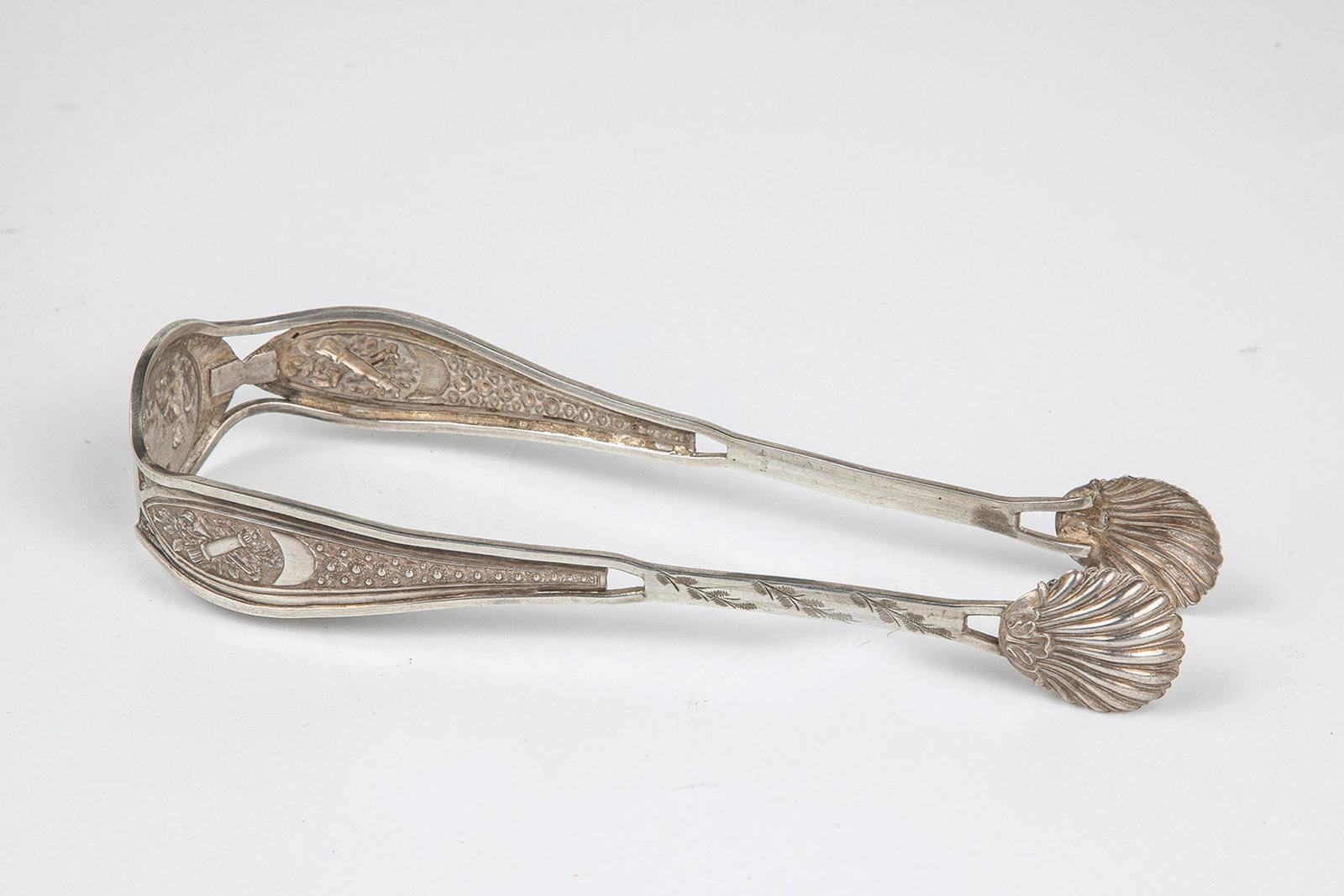 Sugar tongs: Sugar tongs probably German, late 19th century silver. The handling is partly openwork and driven with stylized flowers and a cupidboard scene. The grippers are worked in the shape of scallops. Unmark